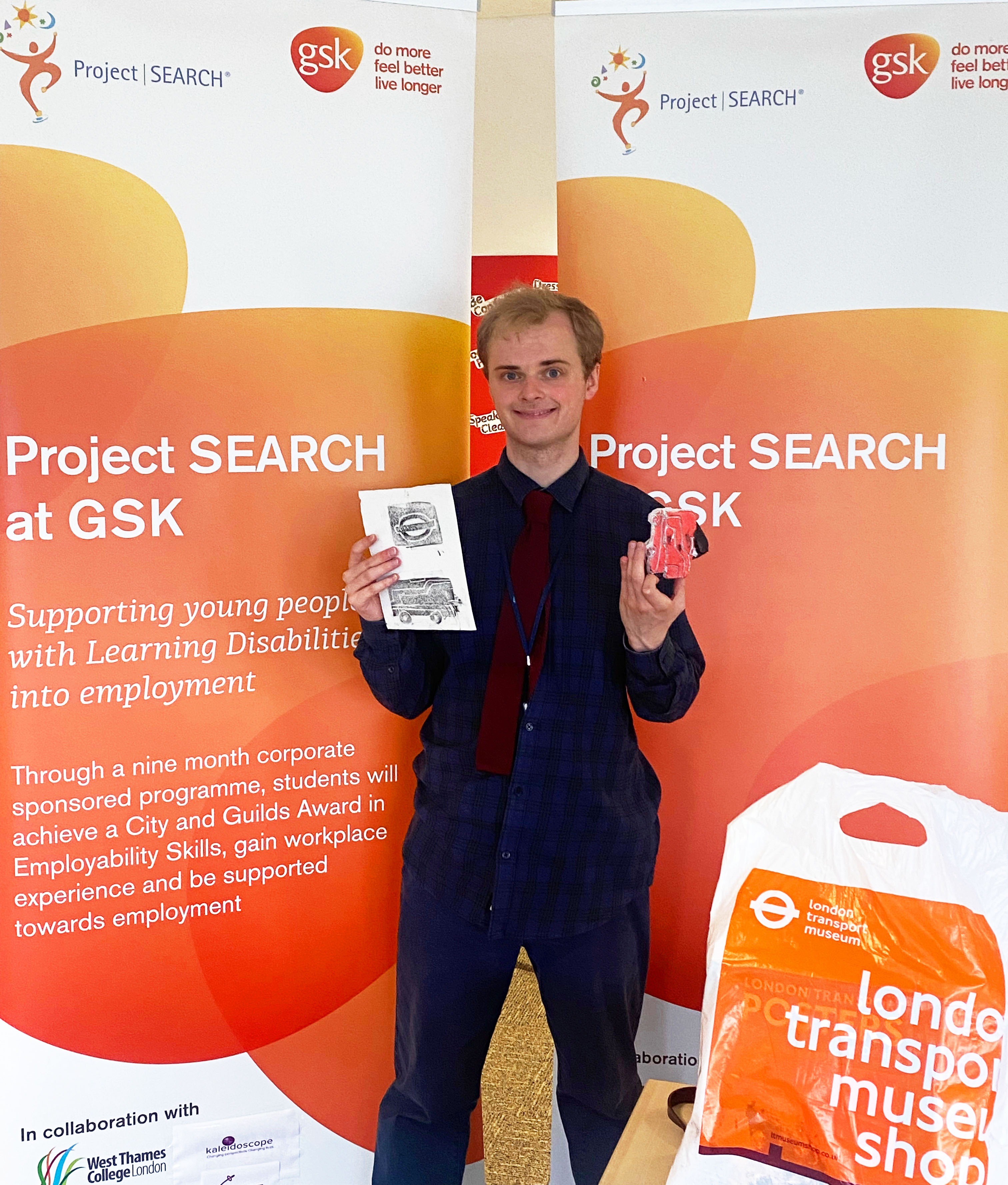 George Goodlake holding his poster design up in front of a GSK banner